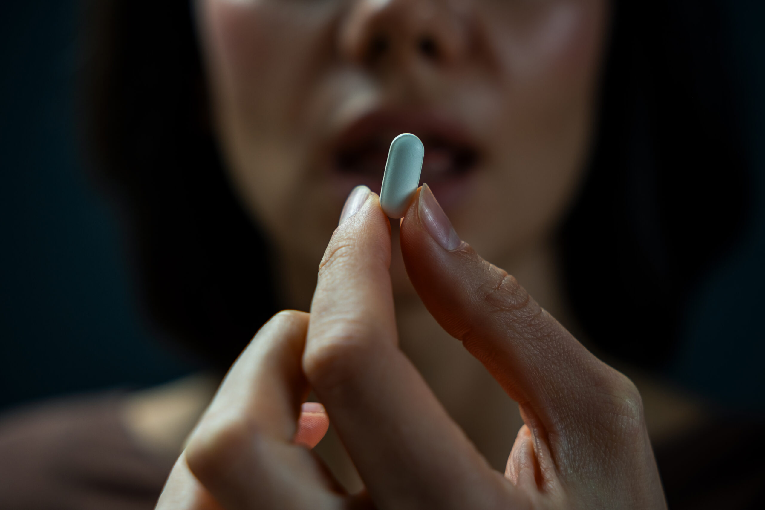 A woman holds a white tablet in dark setting, symbolizing drug addiction and the emotional tension behind substance use.