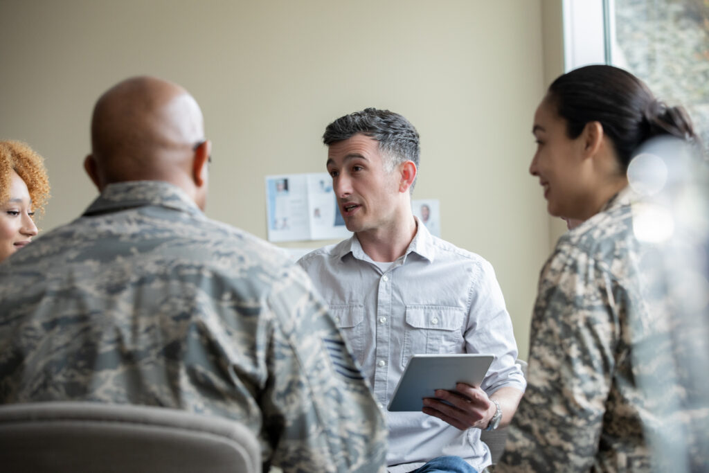 Adult male counselor speaking to multi cultural group of soldiers during therapy session