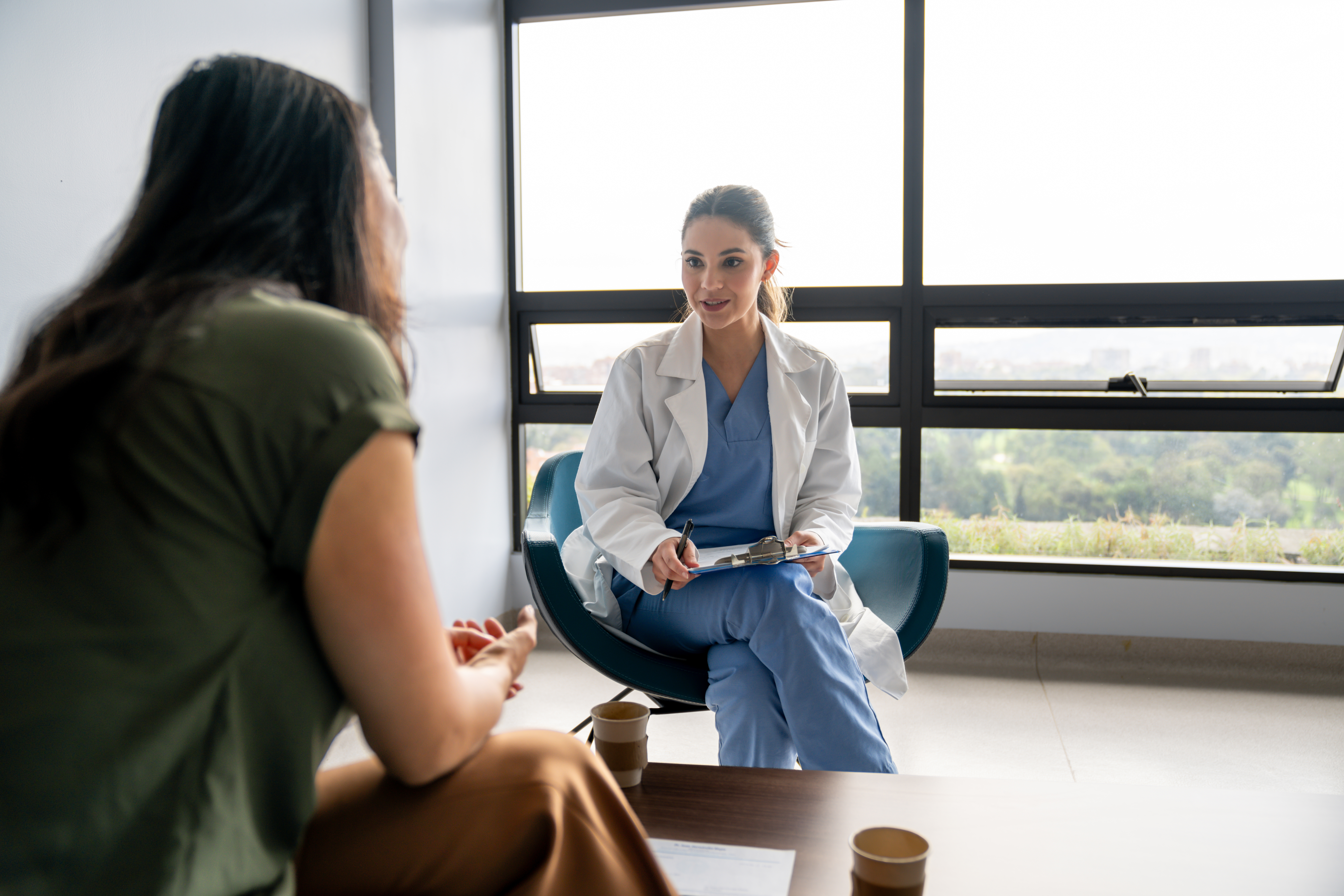 Female doctor talking to a patient in a consultation at the hospital while taking notes on a clipboard