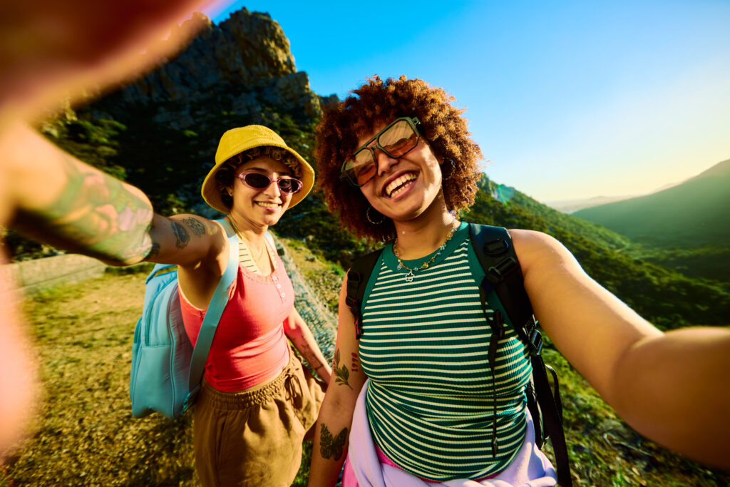 Two happy young women hikers taking a selfie with mountain peak in the background