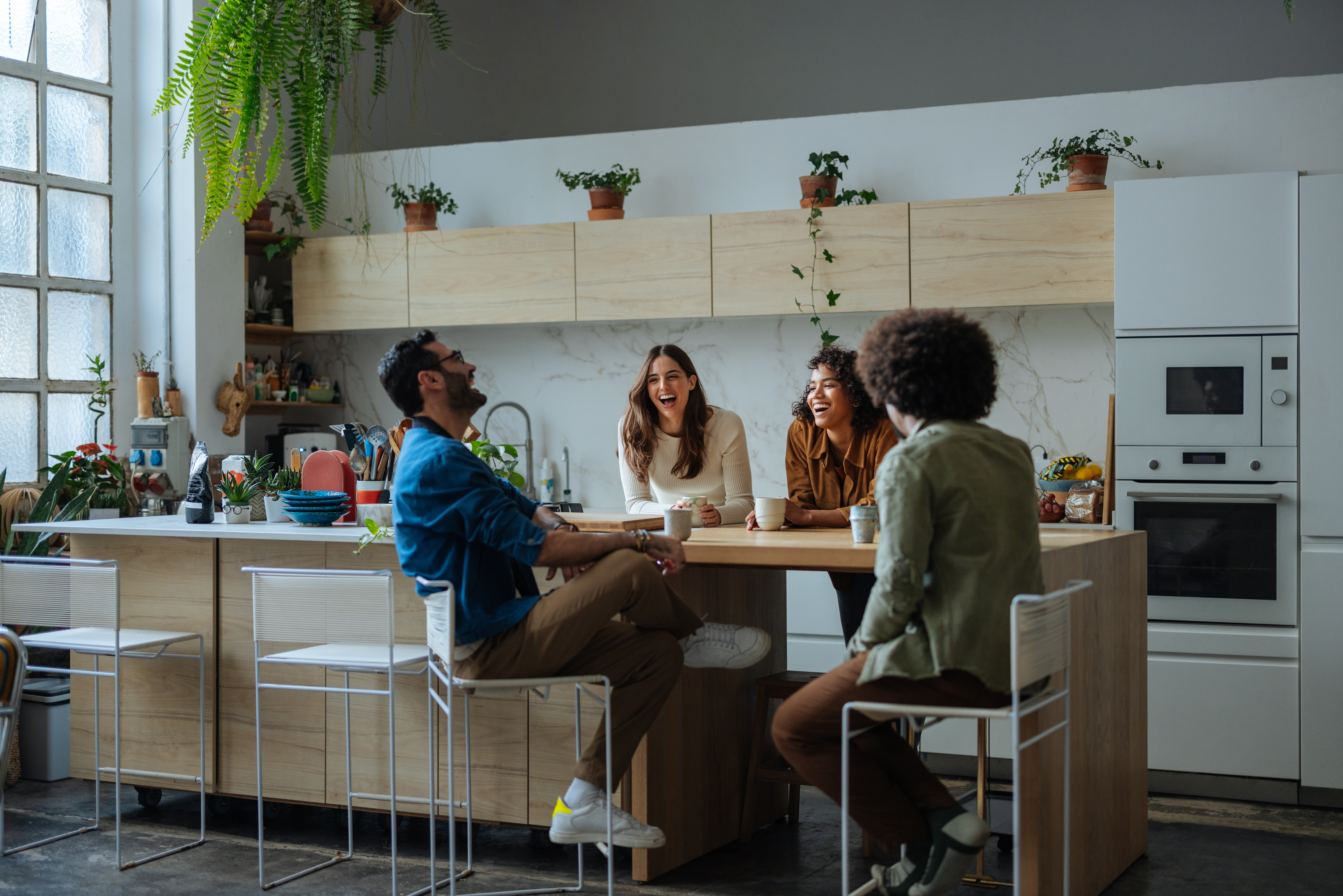 Four friends are enjoying their time together in a modern kitchen, laughing and talking while sitting at the counter
